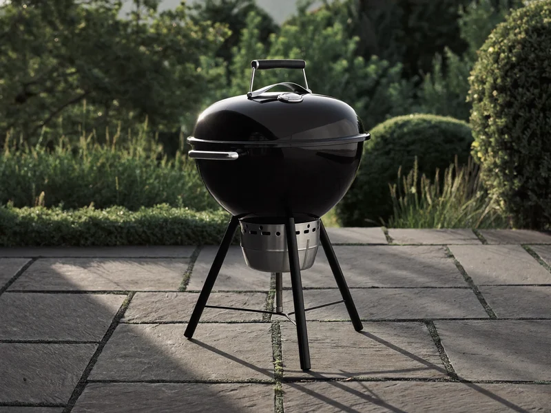 Okrągły czarny grill węglowy z pokrywą na kamiennym patio
